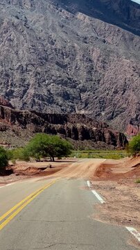 Point of view video driving forward on an empty road towards red gigantic rocky mountains in Salta, Argentina. Sunny weather, scenic landscape. Concept of road trip 