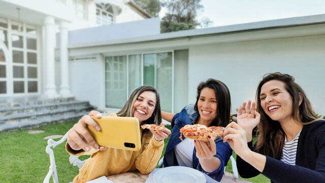 Diverse friends having fun eating vegan pizza at home patio - Young women taking selfie picture together