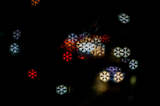 Abstract snowflake shaped bokeh lights glowing against a pitch black background. Festive holiday texture for winter, Christmas, and New Year designs.