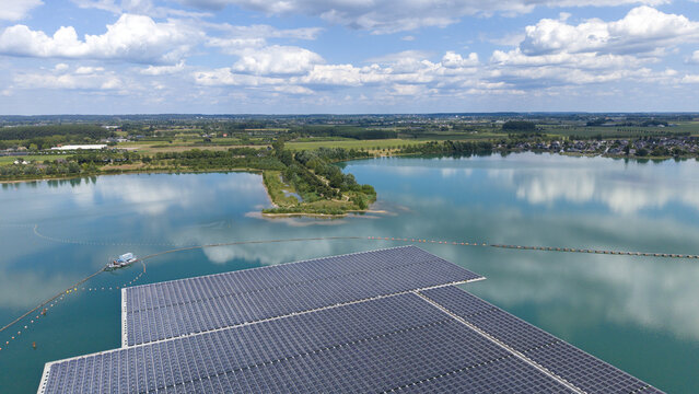 Aerial view of the floating solar farm on Lingemeer lake, surrounded by lush greenery and fields under a blue sky with clouds in Buren, Gelderland, Netherlands.