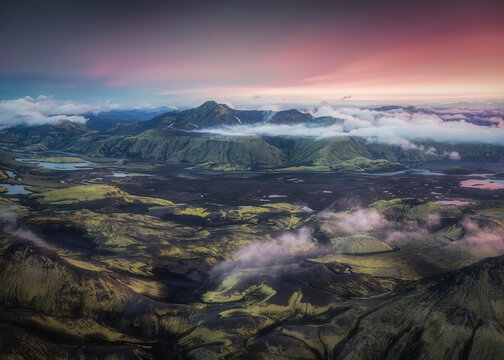Aerial view of Skafta river winding through moss-covered lava fields and volcanic mountains under a vibrant sunset sky in Skaftarhreppur, Iceland.