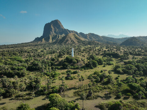Aerial view of the Nuca Molas lighthouse standing amidst a vast landscape of palm trees and rolling hills under a clear blue sky in Satar Mese Barat, East Nusa Tenggara, Indonesia.