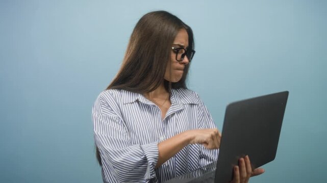 Woman holds laptop and taps keyboard with her hand in studio; concentration problem solving frustration.