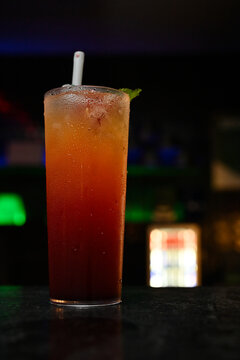 refreshing layered tropical cocktail in highball glass close up, colorful iced drink with straw on dark bar counter with bokeh lights, vibrant night life beverage photography with copy space