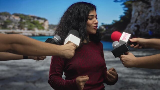 Woman speaks into multiple handheld microphones on a beach with arms holding mics close to her face; anxiety media pressure.
