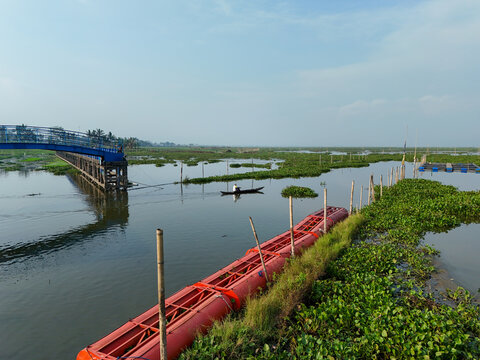 Aerial view of a small boat departing from a dock on Rawa Pening lake, featuring water hyacinths and red floating structures Waduk Rawapening, Central Java, Indonesia.