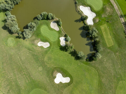 Aerial view of a golf course featuring green fairways, sand bunkers, and water hazards surrounded by trees in Munich, Bavaria, Germany.
