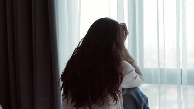 Mental health problems and depression concept: Rear view of a depressed female sitting on a bed, feeling isolated and sad at home