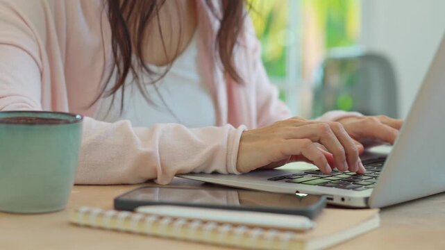 Cropped shot of a thoughtful Asian woman working on a laptop at a bright home desk