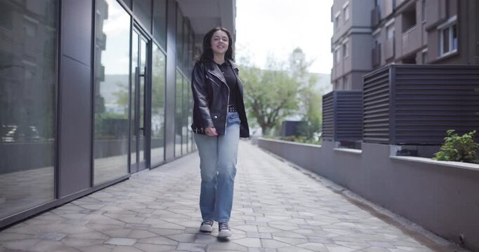 Young woman walking confidently in urban setting, stylish outfit and casual jeans
