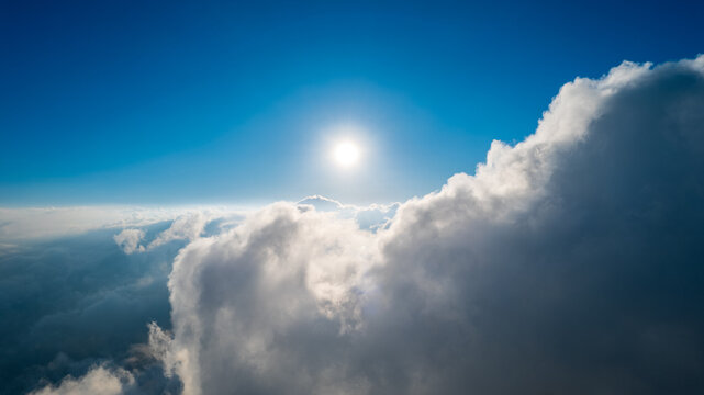 Aerial view of bright sun shining above a thick layer of white clouds in a clear blue sky over Bajawa, Nusa Tenggara Timur, Indonesia.