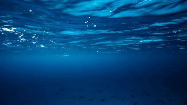 Underwater view of ocean surface with sunlight filtering through blue water and seabed visible below