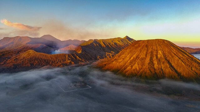 Aerial view of Mount Bromo at sunrise with golden light illuminating the volcanic crater and surrounding sea of clouds in Tosari, East Java, Indonesia.