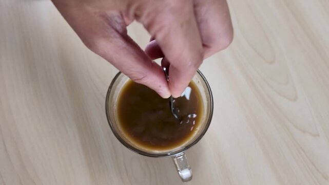 Close Up of Hand Stirring Coffee in Glass Cup