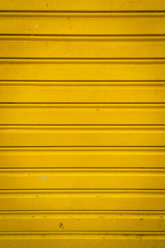 Close-up of a yellow metal rolling shutter with horizontal lines, creating a clean industrial texture background for design and construction concepts.