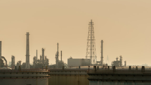 Petroleum refinery complex with industrial towers and storage tanks surrounded by smog. Air pollution, carbon emissions, environmental challenges, energy production and heavy industry.