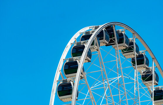 Modern Ferris wheel against blue sky, amusement park attraction for tourism, summer holiday, family entertainment. Amusement ride for travel destination, vacation and funfair entertainment.