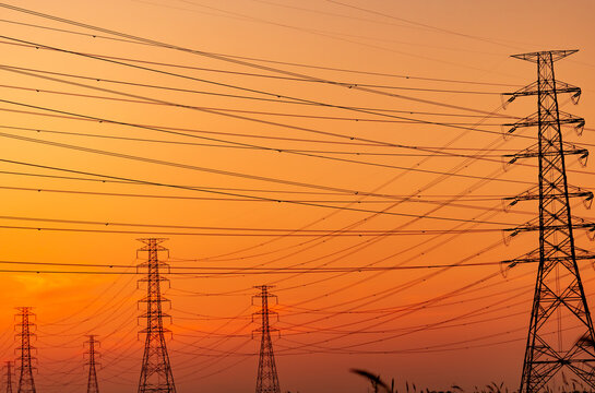 High voltage electricity transmission towers and power lines silhouetted against sunset sky. Electrical grid infrastructure, energy distribution, utility engineering and modern power networks.