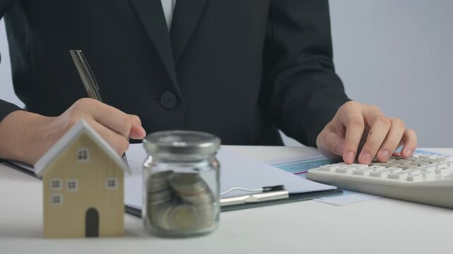 Focused individual manages budget using coin jar and calculator, planning financial strategy to achieve future real estate home ownership goal