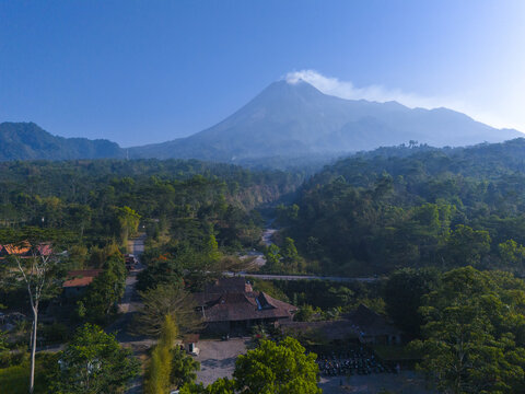 Aerial view of Warung Kopi Merapi nestled in lush greenery with Mount Merapi in the background under a clear blue sky in Kecamatan Cangkringan, Daerah Istimewa Yogya, Indonesia.