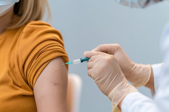 Close up of a gloved hand administering a vaccine injection into a patient arm for immunization and preventive healthcare concepts