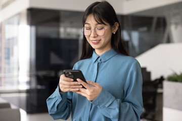 Young Asian businesswoman using smartphone in modern office, checking messages, reading...