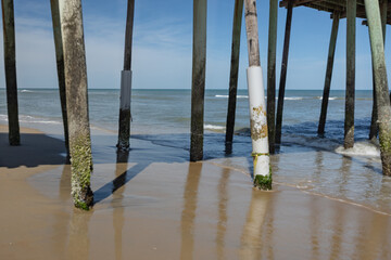 Weathered wooden pilings support a pier in the Atlantic Ocean, taken from the beach under and to the right of the structure.  © Archival Stone Stock