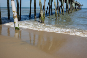 Weathered wooden pilings support a pier in the Atlantic Ocean, taken from the beach under and to the right of the structure.  © Archival Stone Stock