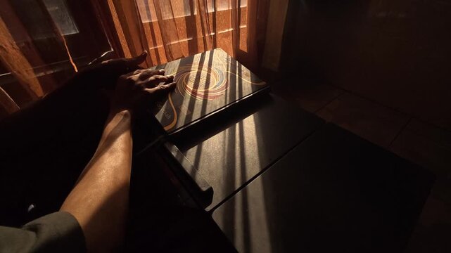 Gresik Indonesia - August 5, 2026: Landscape Side Angle Slow Motion of Person Closing Large Book on Wooden Table in Warm Window Sunlight