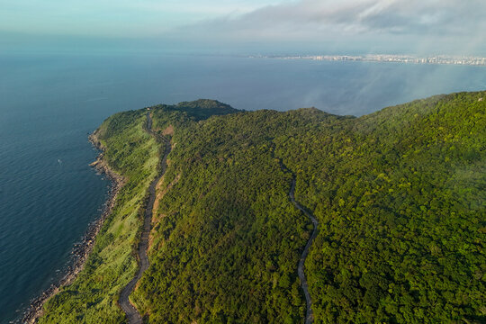 Lush forest covers the steep slopes of Son Tra Peninsula as a coastal road winds past the blue ocean waters on a clear morning in central Vietnam