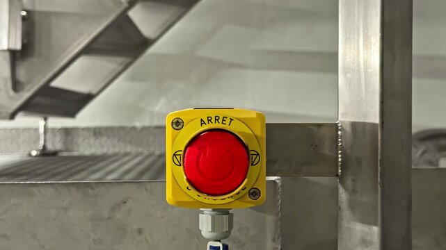 View of an emergency stop button with a red button and yellow housing labeled ARRET mounted on a metal structure in France.