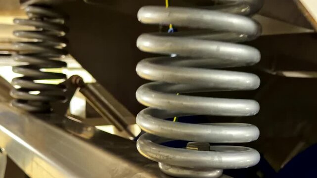 View of a heavy-duty metal coil spring used in a vehicle suspension system, showcasing the industrial design and metallic texture in France.