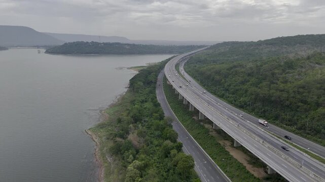 Aerial view of highway running along river and green hills. Transportation, infrastructure, travel and logistics concept
