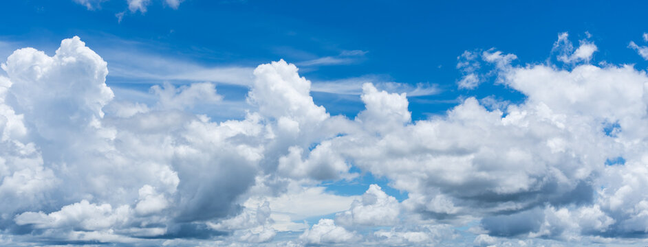 Panoramic view of a bright blue sky filled with fluffy white cumulus clouds and wispy cirrus streaks on a sunny day.