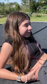 Caucasian teenage girl with long hair experiencing a range of emotions from happiness to sadness while lying on a trampoline outdoors during a sunny day in her backyard