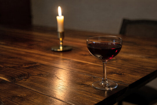 Red Wine Coupe Glass by Candlelight on Wooden Table
