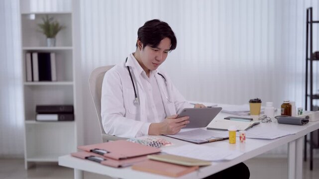 Young Asian male doctor reviewing patient data on digital tablet at modern medical office desk