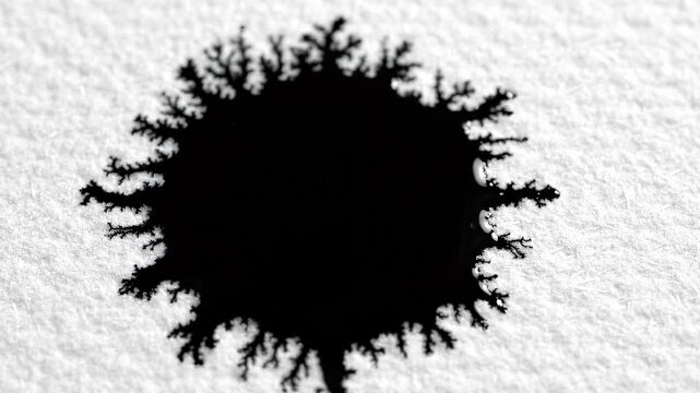 Black ink drop spreading on white textured paper. Fluid dynamics and abstract liquid movement. Artistic demonstration of capillary action and absorption process.