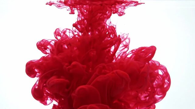 Red ink drop swirling in clear water. Liquid dye cloud spreading to create abstract shapes. Chemical reaction and fluid motion experiment for scientific display.