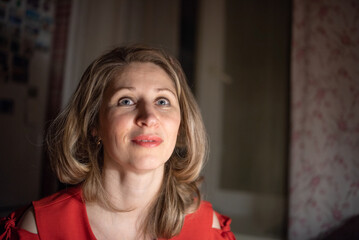 Thoughtful caucasian woman in red dress sitting at a bar or cafe at night, holding a smartphone, with a blurred glass of wine or cocktail in the foreground with dim lighting. © shymar27