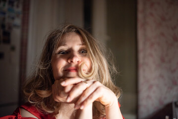 Thoughtful caucasian woman in red dress sitting at a bar or cafe at night, holding a smartphone, with a blurred glass of wine or cocktail in the foreground with dim lighting. © shymar27