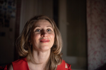 Thoughtful caucasian woman in red dress sitting at a bar or cafe at night, holding a smartphone, with a blurred glass of wine or cocktail in the foreground with dim lighting. © shymar27