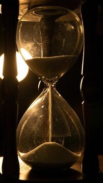 A vintage wooden hourglass with flowing sand captured in dramatic low light with a warm glow.
