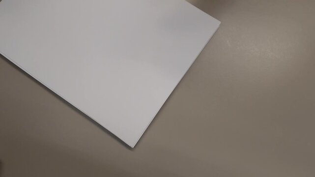 Top view of a small stack of blank papers with paper clips falling onto them on an office desk, representing organization, documentation and workplace tasks.