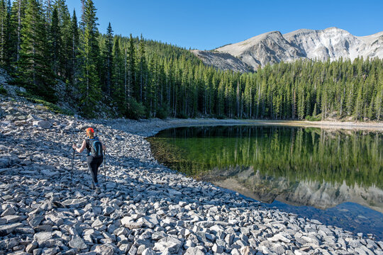 Woman explores shore of second Thomas Lake in Maroon Bells-Snowmass Wilderness in White River National Forest on calm clear summer morning.