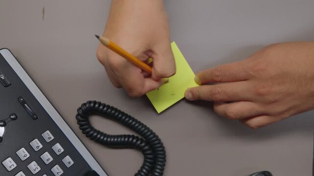 Overhead close-up of a hand erasing pencil writing from a sticky note with an eraser, representing editing, correction and office productivity.