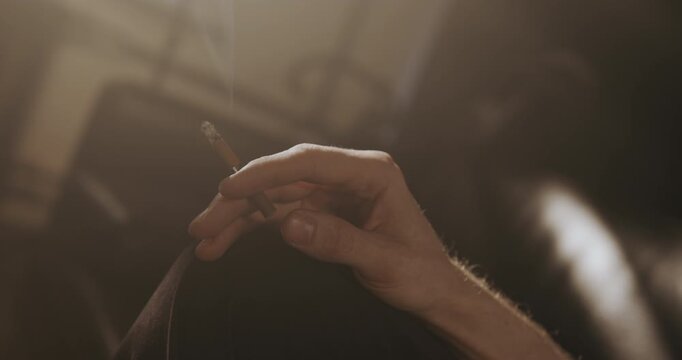 Close-up of a hand holding a lit cigarette as it moves out of the frame and then returns.