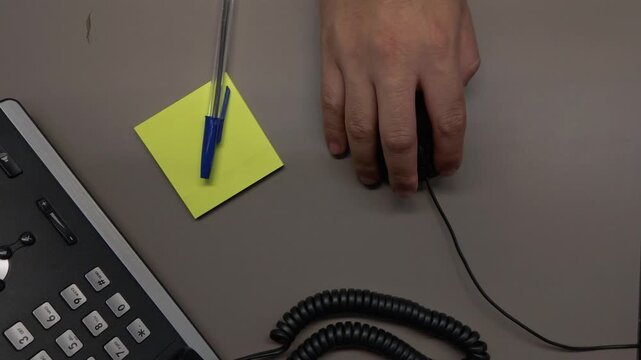 Overhead view of a hand using a computer mouse with natural clicking movements on an office desk featuring yellow sticky notes and a blue pen.