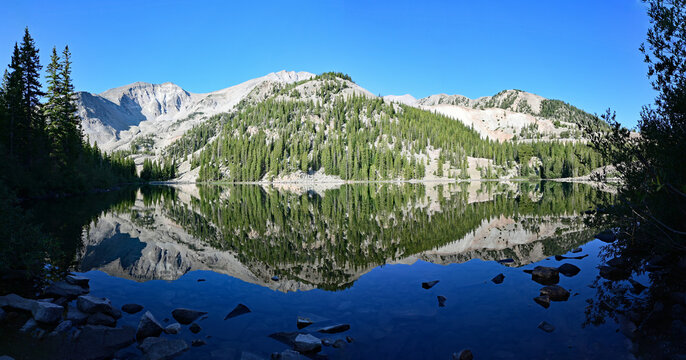Panorama of Mount Sopris reflected in calm water of Thomas Lake in Maroon Bells-Snowmass Wilderness near Carbondale, Colorado on sunny summer morning.