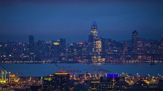 View of the illuminated San Francisco skyline with the Salesforce Tower and Bay Bridge visible across the water in San Francisco, California, United States.